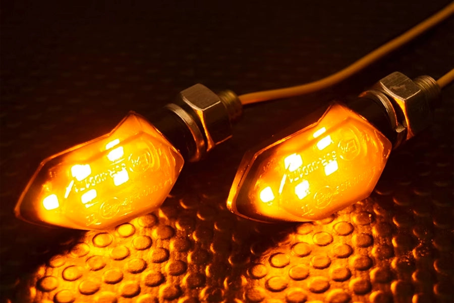 Kaksi Mini LED-vilkkua, joissa on oranssit valot päällä, asetettuna mustalle, kuvioidulle pinnalle.